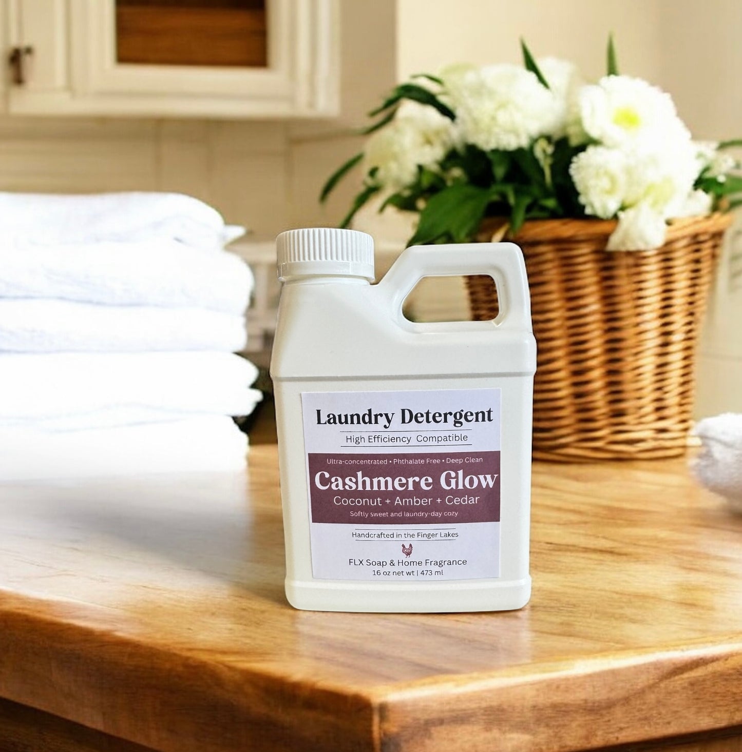 Laundry detergent bottle labeled 'Cashmere Glow' on a wooden surface with folded towels and flowers in the background.