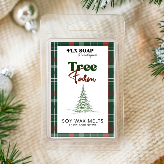 Packaged soy wax melts with 'Tree Farm' label surrounded by Christmas decorations on a textured fabric background.