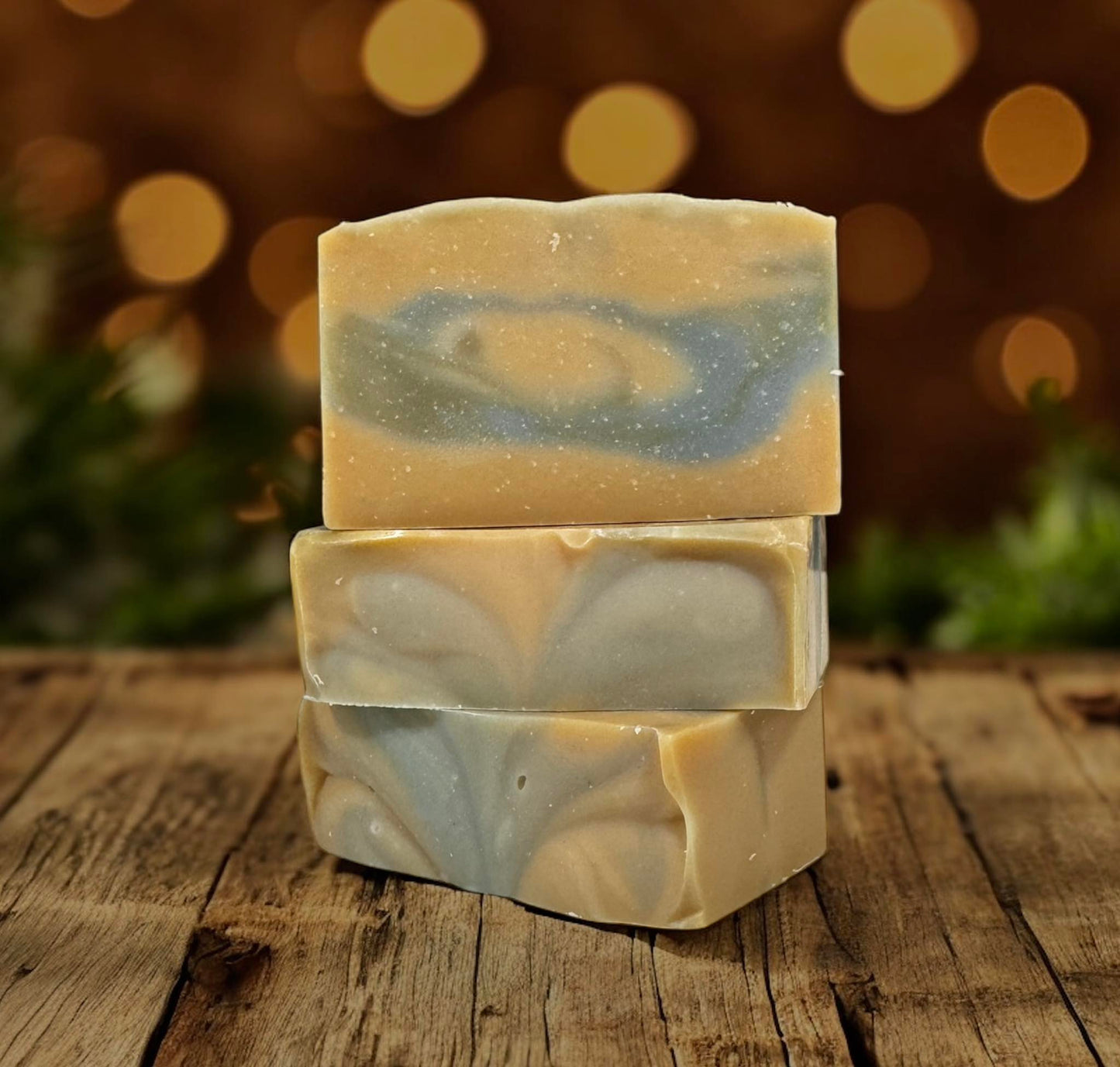 Three bars of soap with a swirling pattern stacked on a wooden surface with a blurred bokeh background.